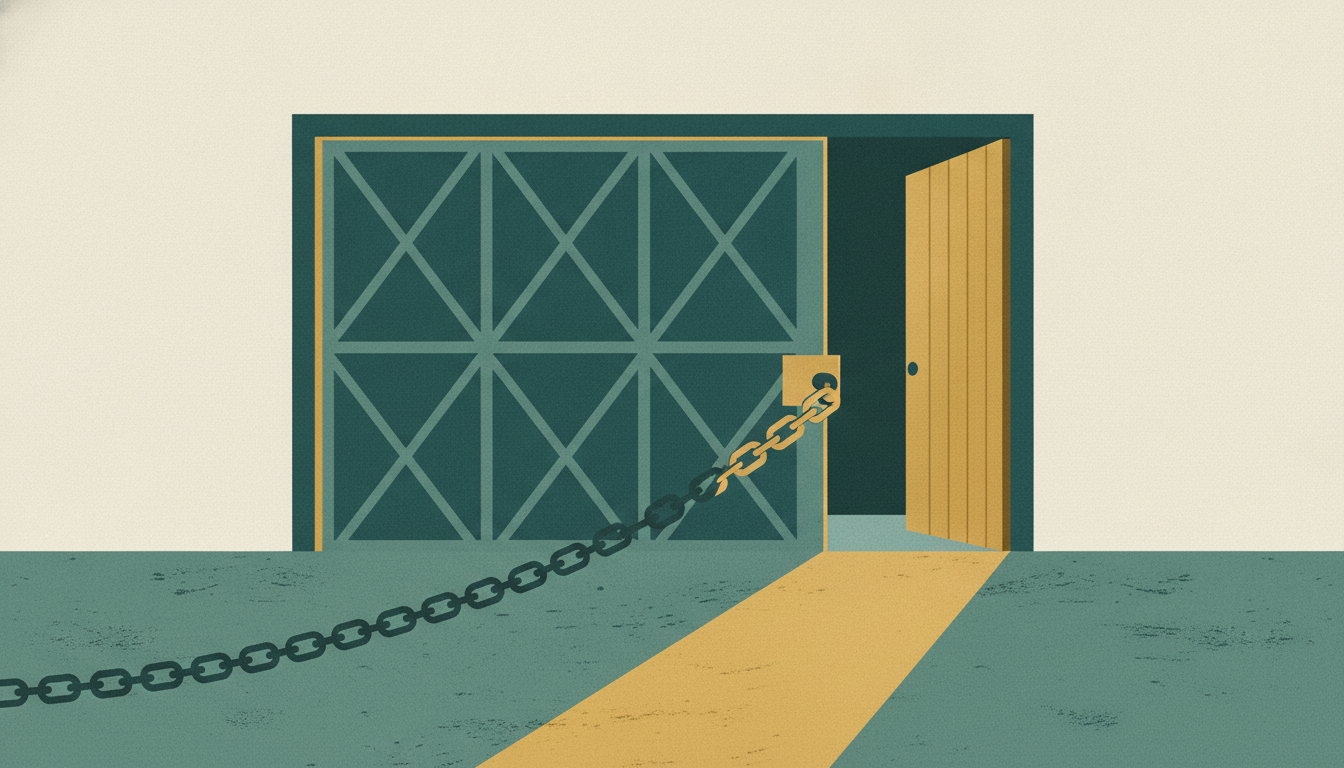 A narrow wooden door stands ajar beside a chained gate, spilling warm amber sunlight across a concrete floor.